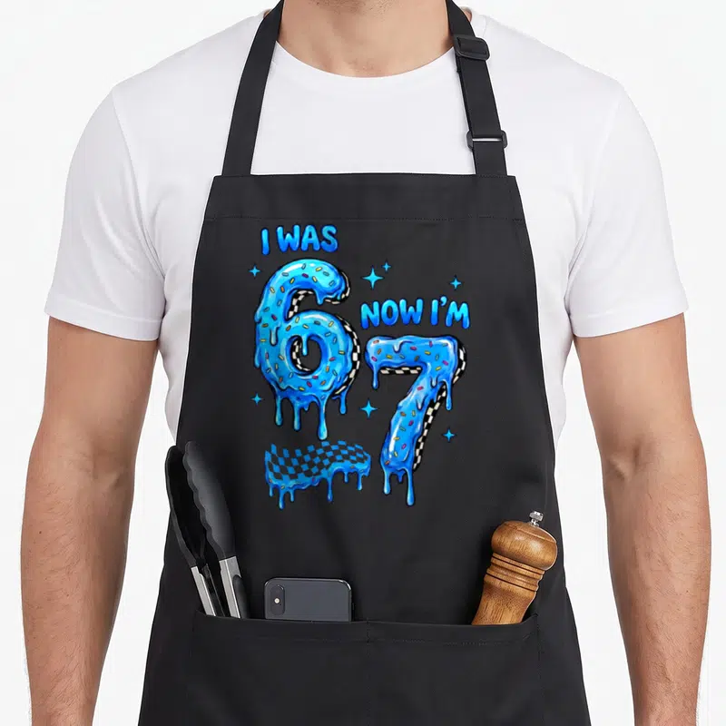 Drip checkered apron - Blue dripping numbers 6 and 7 with checkerboard pattern and I WAS NOW I'M text — shown on a black cotton canvas apron against a white background