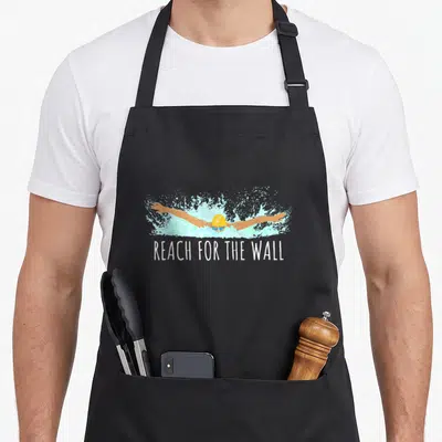 Gear swimming apron - Cartoon swimmer in yellow cap and blue goggles reaching forward in a light blue splash above — shown on a black cotton canvas apron against a white background
