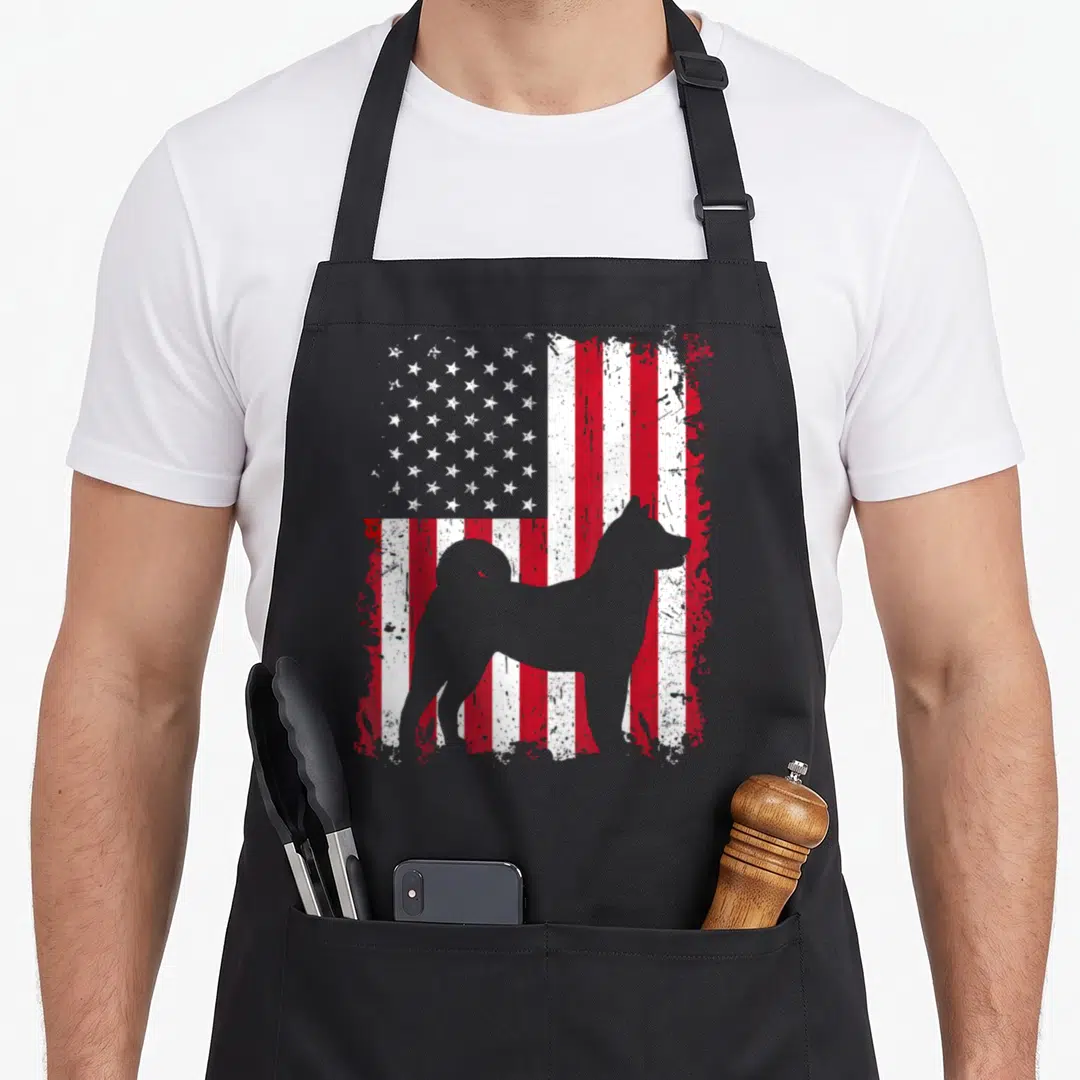 Akita 4th of july apron - Grey dog silhouette standing before distressed red white American flag pattern — shown on a black cotton canvas apron against a white background