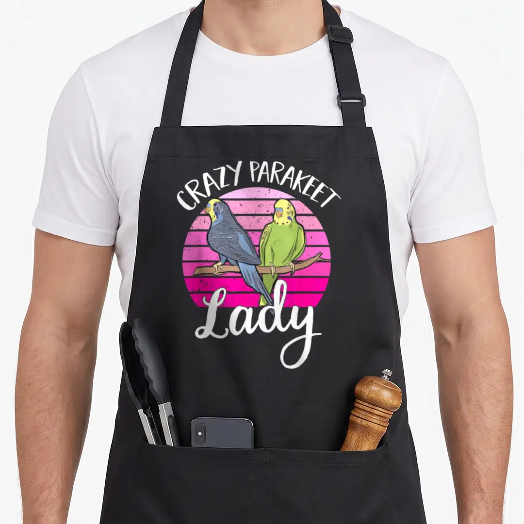 Parakeet pet apron - Two parakeets on a branch before a striped pink circle with white text reading CRAZY PARAKEET Lady — shown on a black cotton canvas apron against a white background