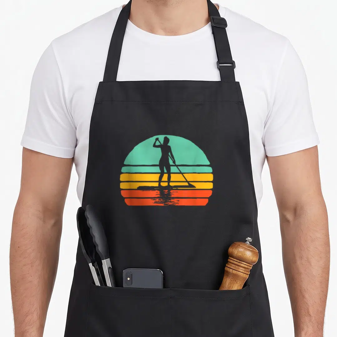 Sup paddleboard apron - Grey woman paddleboard silhouette over teal yellow orange red striped sun — shown on a black cotton canvas apron against a white background