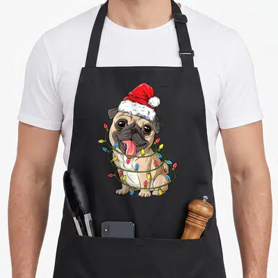 Pug christmas tree apron - Cartoon tan pug in red santa hat wrapped in blue, green, yellow, and red Christmas lights — shown on a black cotton canvas apron against a white background