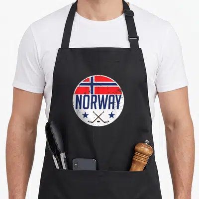 Norway nordic apron - Distressed circular Norway flag emblem with blue text and crossed hockey sticks and puck — shown on a black cotton canvas apron against a white background