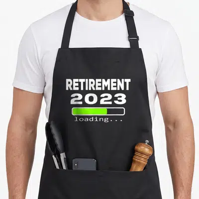 Loading retirement apron - White text reading RETIREMENT 2023 above a green loading bar and small loading label — shown on a black cotton canvas apron against a white background