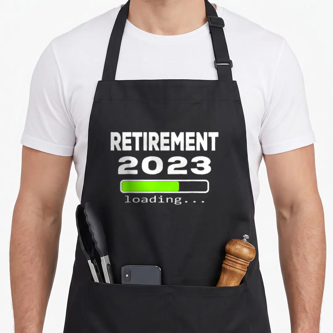 Loading retirement apron - White text reading RETIREMENT 2023 above a green loading bar and small loading label — shown on a black cotton canvas apron against a white background