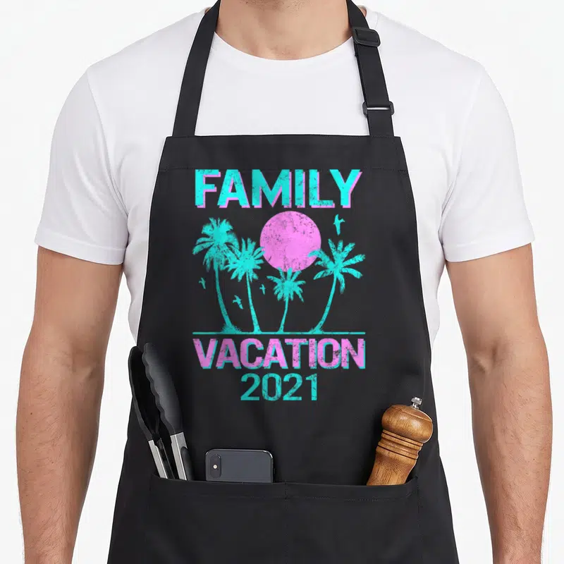 Mode family aprons - Retro pink sun and cyan palm trees with FAMILY VACATION 2021 text — shown on a black cotton canvas apron against a white background