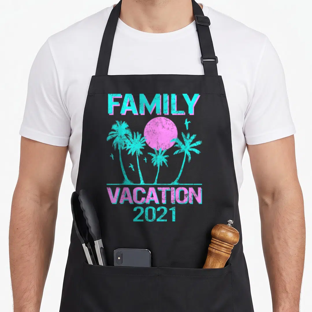 Mode family aprons - Retro pink sun and cyan palm trees with FAMILY VACATION 2021 text — shown on a black cotton canvas apron against a white background