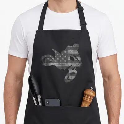 Dirt american flag apron - Grey and white distressed flag pattern filling a motocross rider silhouette on a black bib — shown on a black cotton canvas apron against a white background