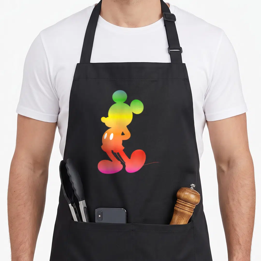 Gradient silhouette rainbow apron - Mickey Mouse silhouette filled with green yellow orange red purple gradient colors — shown on a black cotton canvas apron against a white background