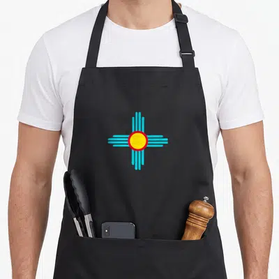 Modern mexico apron - Yellow circle red border four groups of four cyan lines radiating outward — shown on a black cotton canvas apron against a white background