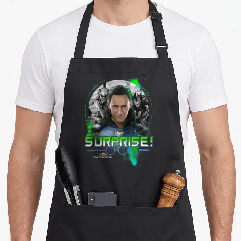 Ragnarok collectible apron - Loki centered in lime green circle with Thor Hela behind and SURPRISE text below — shown on a black cotton canvas apron against a white background