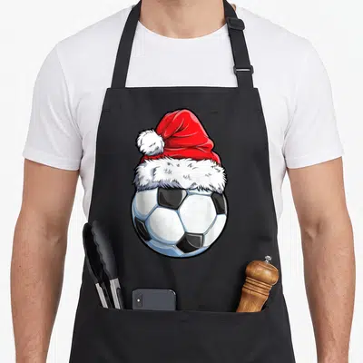 Soccer santa aprons - Cartoon soccer ball wearing a red and white Santa hat in black, white, and red art style — shown on a black cotton canvas apron against a white background