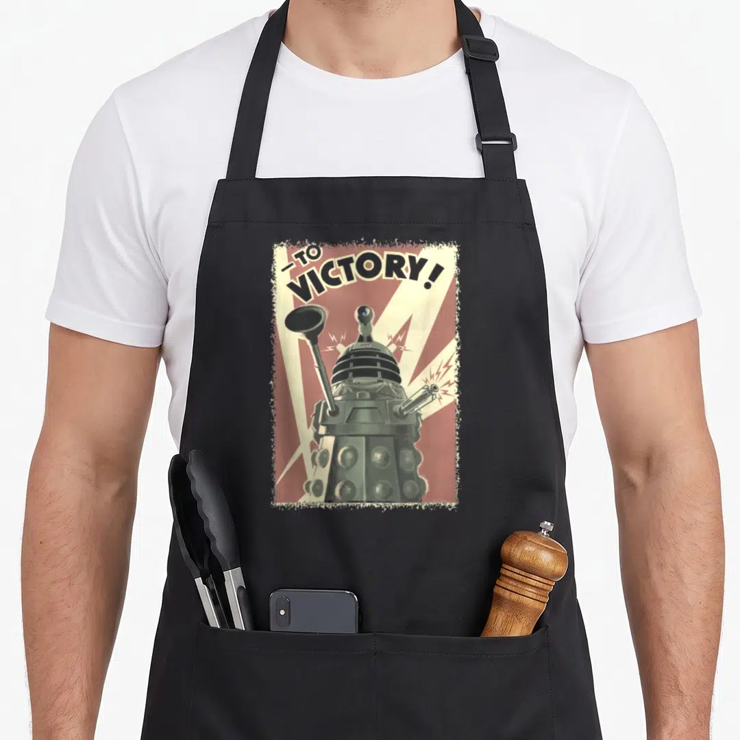 Propoganda collectible apron - Dalek centered in red frame with cream rays and TO, VICTORY! text in distressed style — shown on a black cotton canvas apron against a white background