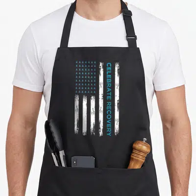 Drug sobriety apron - Distressed flag with light blue ribbons and vertical CELEBRATE RECOVERY text — shown on a black cotton canvas apron against a white background