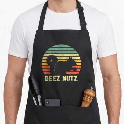 Deez squirrel aprons - Black squirrel silhouette in front of striped retro sun with DEEZ NUTZ text below — shown on a black cotton canvas apron against a white background