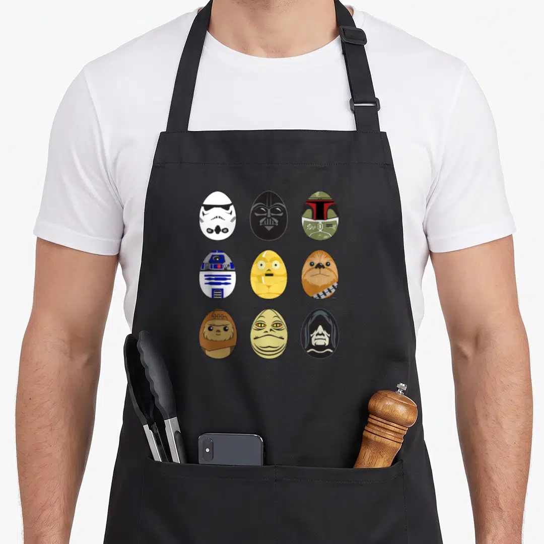 Original easter egg apron - Nine cartoon egg portraits of characters in white, black, yellow, brown, green, and blue — shown on a black cotton canvas apron against a white background