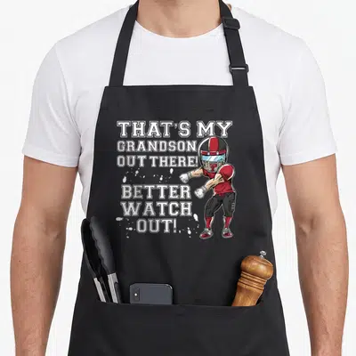 Grandson football grandma aprons - Cartoon football player in red helmet overlapping white stacked text THATS MY — shown on a black cotton canvas apron against a white background