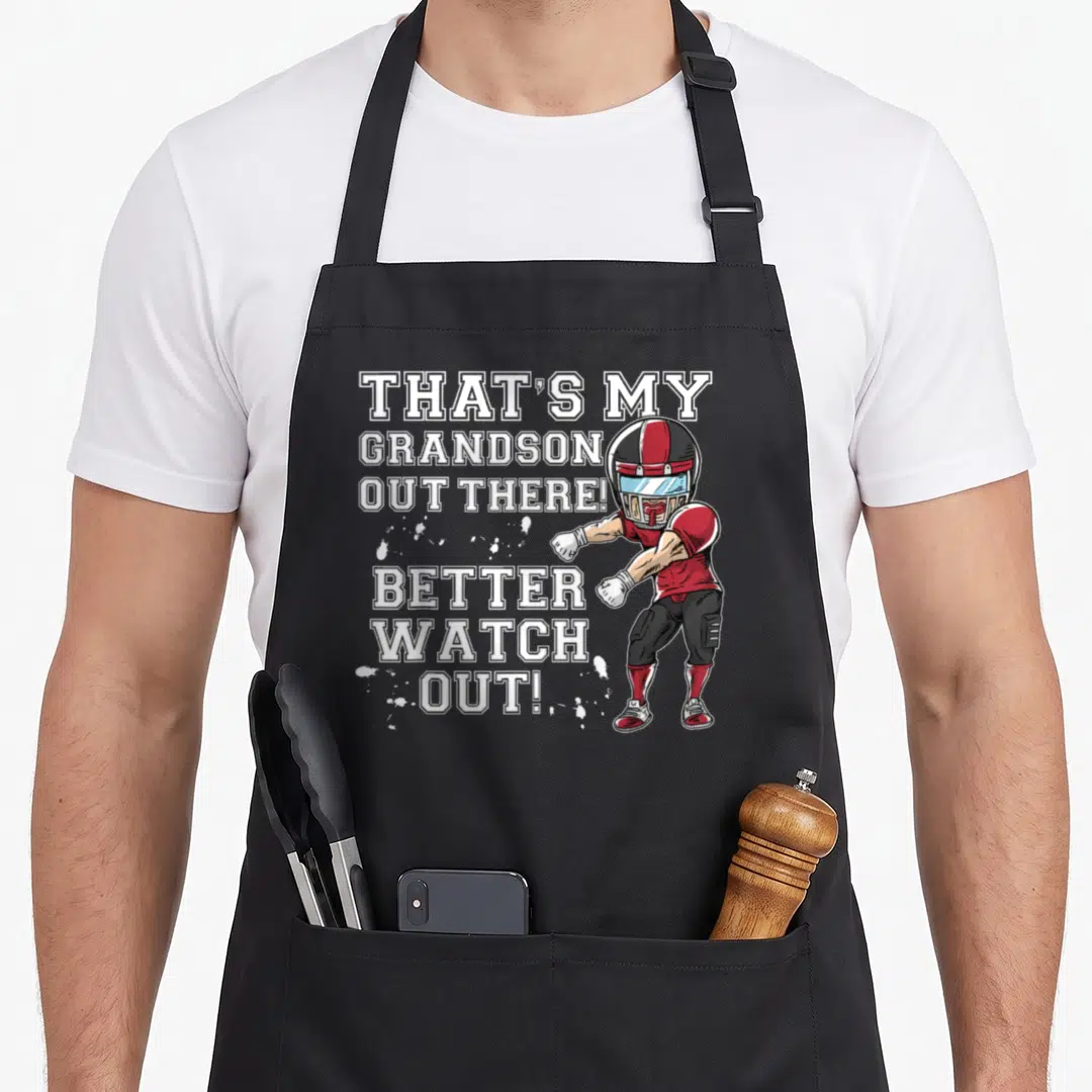 Grandson football grandma aprons - Cartoon football player in red helmet overlapping white stacked text THATS MY — shown on a black cotton canvas apron against a white background