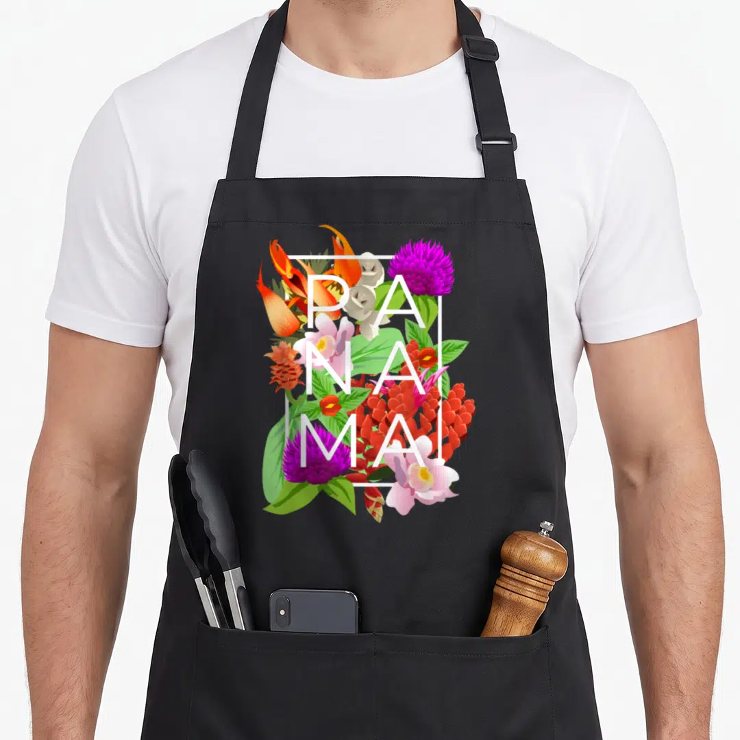 Panama pride apron - White PANAMA text over orange heliconia, purple globe amaranth, and green leaves in a rectangular — shown on a black cotton canvas apron against a white background