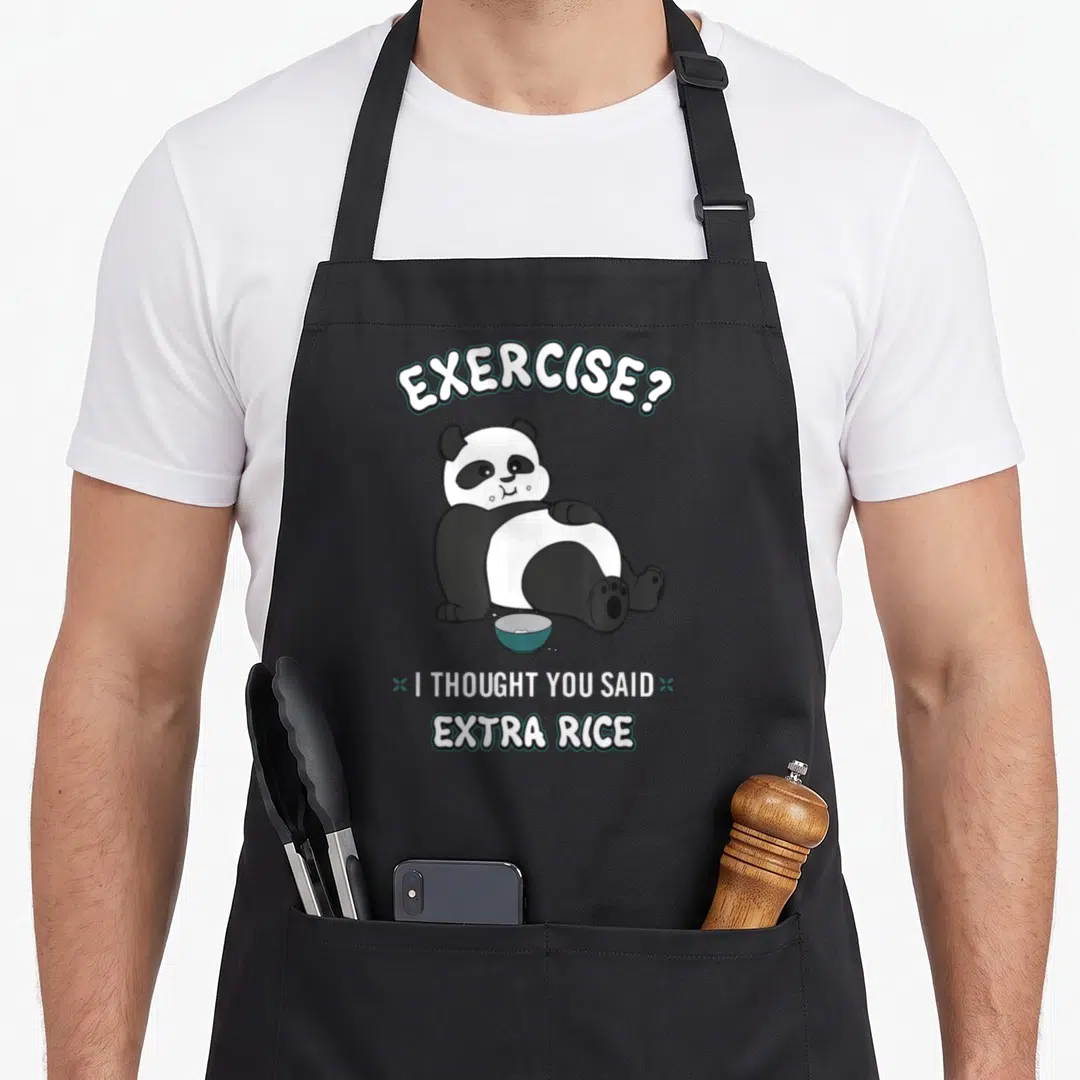 Bcc bear apron - Cartoon panda sitting with blue rice bowl under arched text reading Exercise I Thought You Said Extra — shown on a black cotton canvas apron against a white background