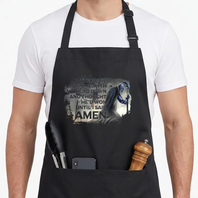 Won devil's apron - Kneeling knight with sword and stacked prayer text reading until I said AMEN in distressed blue — shown on a black cotton canvas apron against a white background