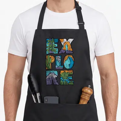 Explore modern apron - Word EXPLORE filled with cartoon mountains trees and water in blue green orange purple — shown on a black cotton canvas apron against a white background