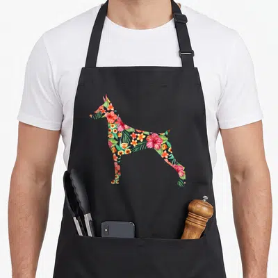 Doberman floral apron - Standing dog silhouette filled with red, green, orange, and pink tropical watercolor flowers — shown on a black cotton canvas apron against a white background
