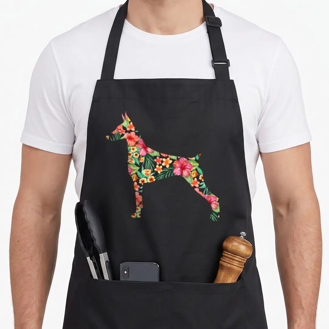 Doberman floral apron - Standing dog silhouette filled with red, green, orange, and pink tropical watercolor flowers — shown on a black cotton canvas apron against a white background