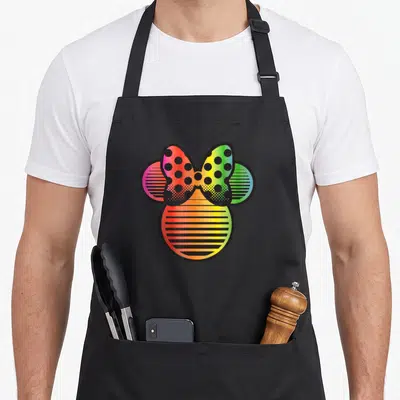 Funny gradient rainbow apron - Minnie Mouse head silhouette with rainbow gradients, dotted bow, and striped ears — shown on a black cotton canvas apron against a white background