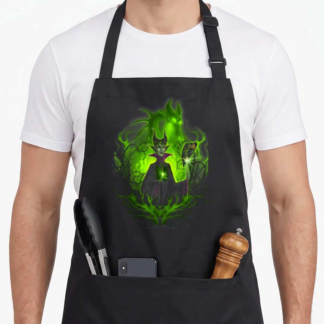 Dark beauty apron - Maleficent with glowing dragon, raven on staff, and green thorns in cartoon style — shown on a black cotton canvas apron against a white background