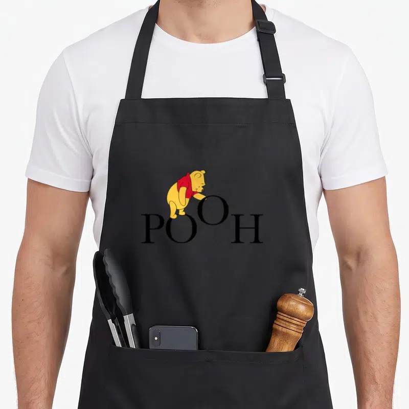 Funny letter novelty apron - Winnie the Pooh in red shirt standing on black POOH letters — shown on a black cotton canvas apron against a white background