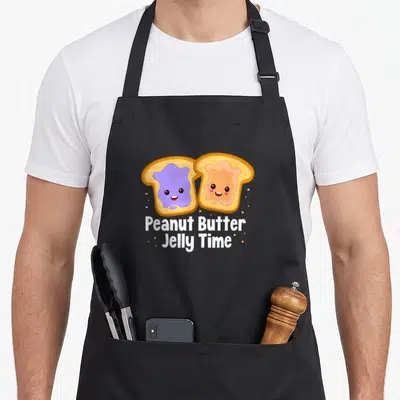 Cool peanut butter apron - Two cartoon toast slices with purple and tan spreads, white text below, tan dots scattered — shown on a black cotton canvas apron against a white background