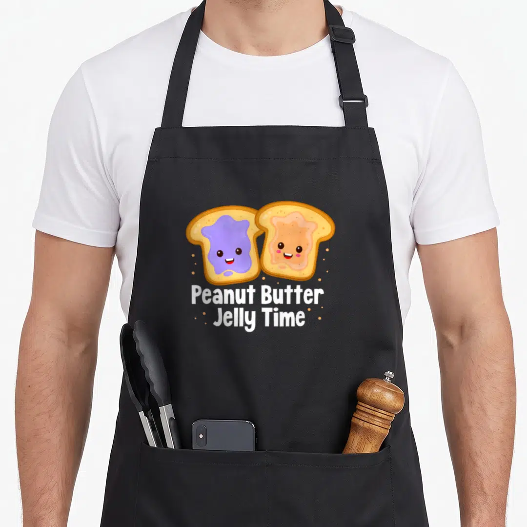 Cool peanut butter apron - Two cartoon toast slices with purple and tan spreads, white text below, tan dots scattered — shown on a black cotton canvas apron against a white background
