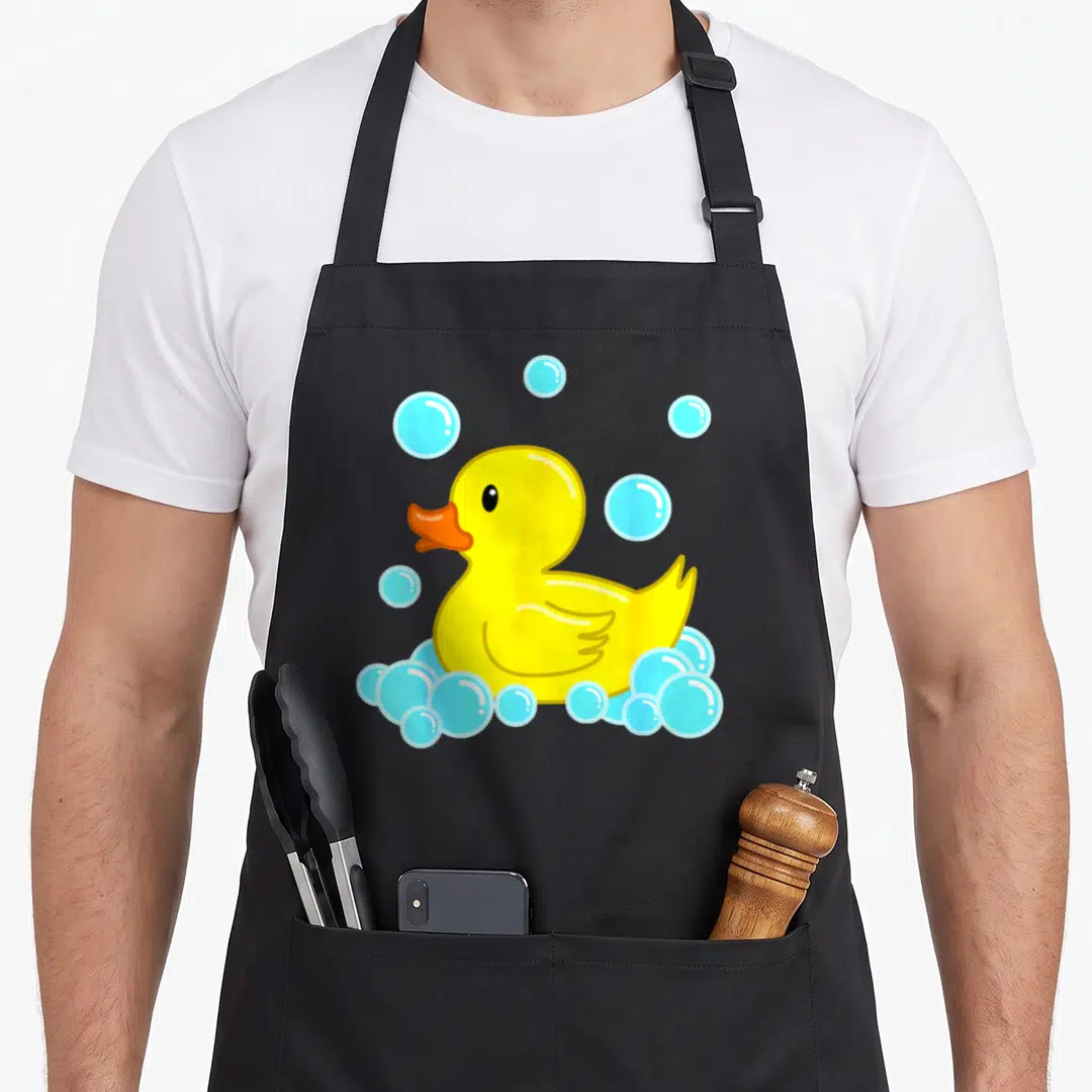 Duckie duck apron - Yellow cartoon rubber duck with orange beak and light blue soap bubbles — shown on a black cotton canvas apron against a white background