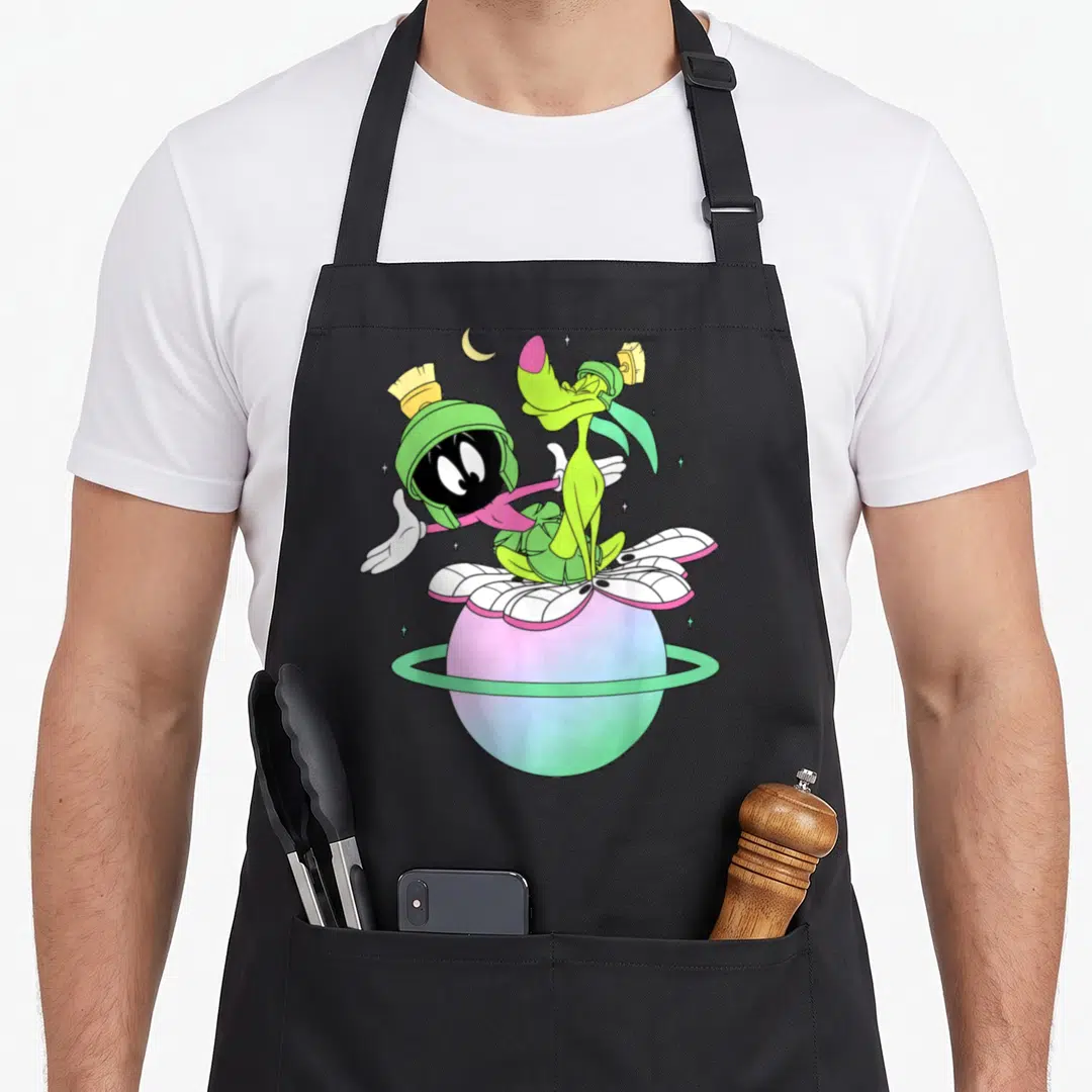 Martian k apron - Two cartoon characters on a colorful ringed planet with a crescent moon and stars — shown on a black cotton canvas apron against a white background
