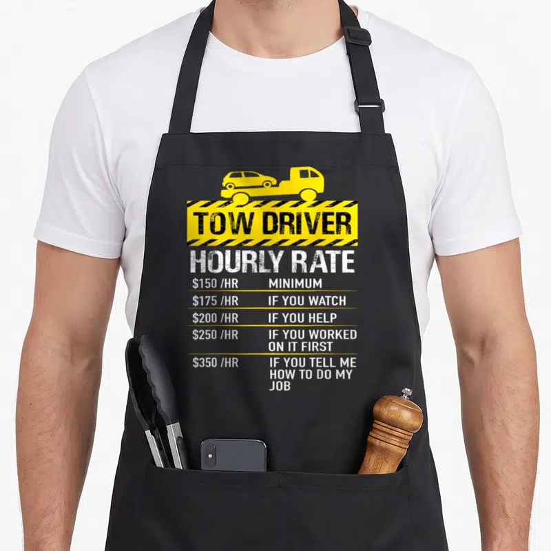 Rate truck apron - Yellow tow truck graphic with hourly rate price list in black and white text — shown on a black cotton canvas apron against a white background