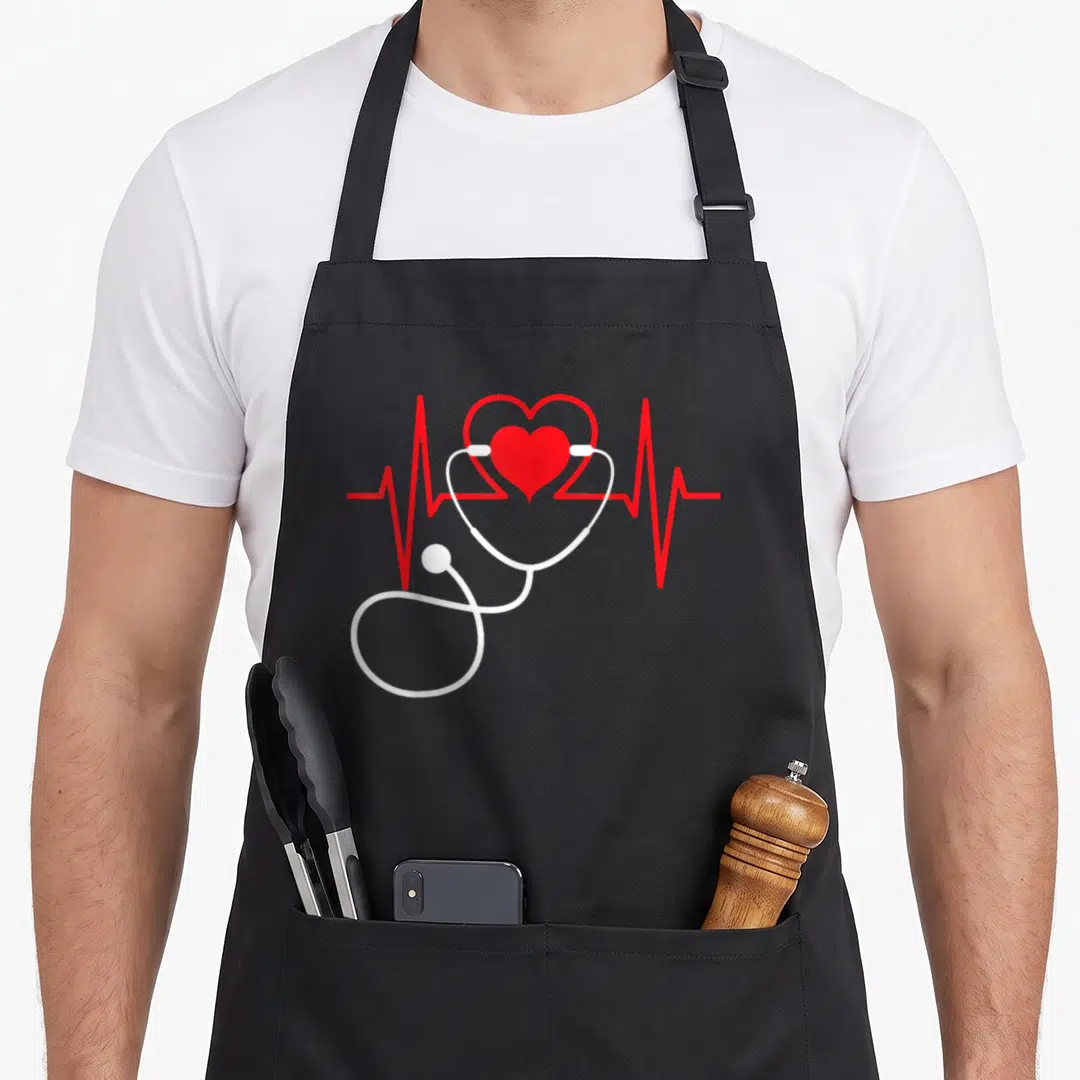 Medical nurse apron - Red heart overlapping white stethoscope with red EKG line on gray background — shown on a black cotton canvas apron against a white background