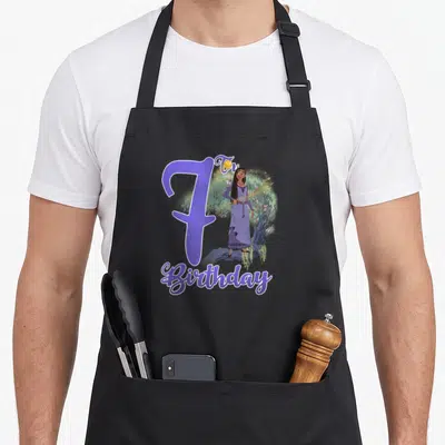 Asha birthday apron - Purple number 7, girl standing by tree, Th Birthday text in cartoon style — shown on a black cotton canvas apron against a white background
