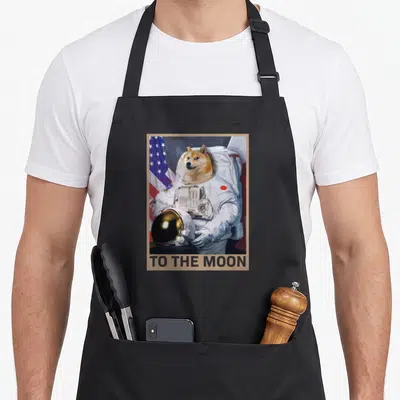 Dogecoin funny lunar apron - Shiba Inu in white spacesuit holding helmet with TO THE MOON text and US flag background — shown on a black cotton canvas apron against a white background