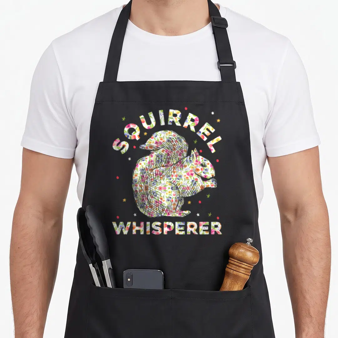 Funny squirrel animal apron - Floral squirrel silhouette with arched SQUIRREL WHISPERER text and scattered stars — shown on a black cotton canvas apron against a white background
