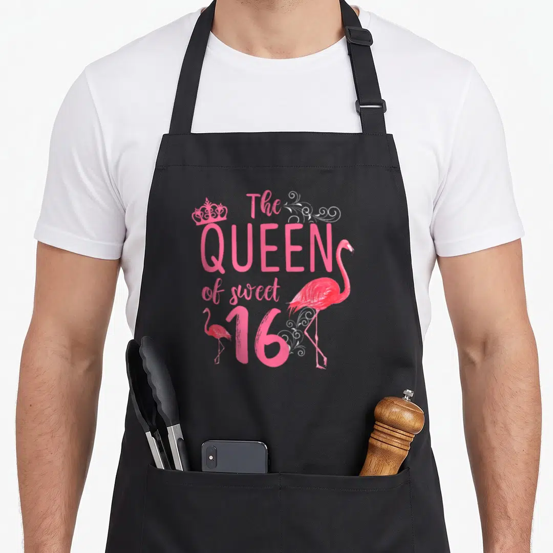 Sixteen flamingo birthday apron - Pink flamingos and crown surrounding The QUEEN of sweet 16 text with white swirls — shown on a black cotton canvas apron against a white background