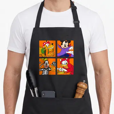 Surprise halloween apron - Mickey, Pluto, Goofy, Donald in costumes holding pumpkin buckets on orange squares — shown on a black cotton canvas apron against a white background