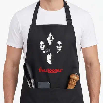 Iggy face apron - four stacked portraits of band members with red the stooges text below — shown on a black cotton canvas apron against a white background
