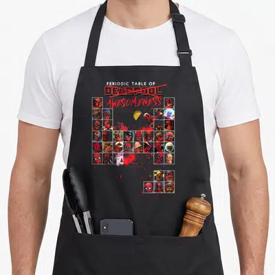 Awesomeness table apron - Deadpool grid with crossed out text, taco, and red blood splatters in cartoon style — shown on a black cotton canvas apron against a white background