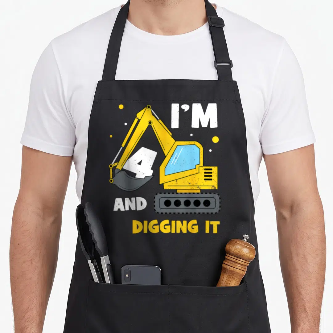 4th excavator birthday apron - Yellow excavator holding white number 4 with I'M 4 AND DIGGING IT text — shown on a black cotton canvas apron against a white background