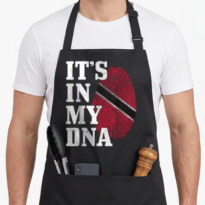 Caribbean trinidad and tobago apron - IT'S IN MY DNA text next to a red fingerprint with a diagonal black and white — shown on a black cotton canvas apron against a white background