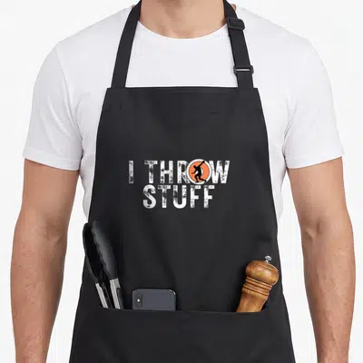 Thrower track apron - I THROW STUFF text with orange circle and black throwing silhouette replacing the letter O — shown on a black cotton canvas apron against a white background