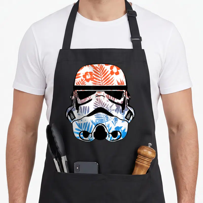 Paradise floral apron - Stormtrooper helmet filled with orange and blue floral pattern — shown on a black cotton canvas apron against a white background