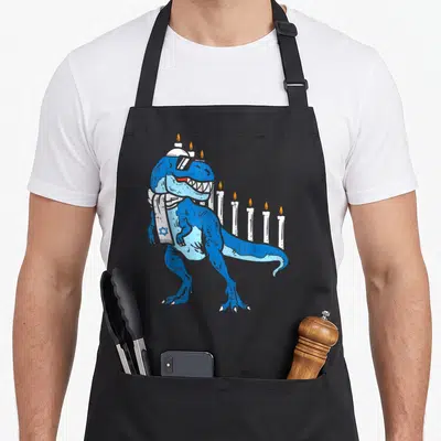 Jew dinosaur apron - Blue T-Rex in tallit acting as menorah with candles on head and back — shown on a black cotton canvas apron against a white background