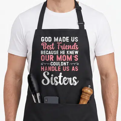 Forever friends apron - Seven lines of white and pink text reading GOD MADE US Best Friends Sisters with swirls — shown on a black cotton canvas apron against a white background